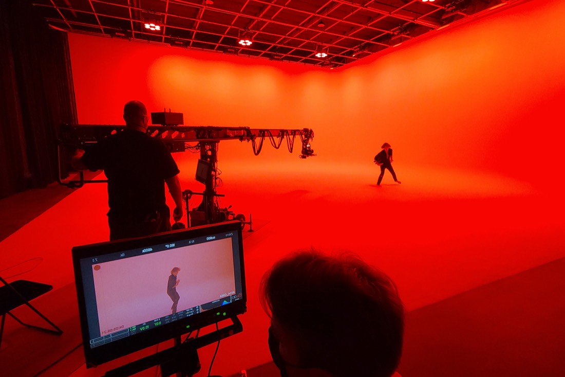 A camera operator on a jib films a performer against a fully red cyc