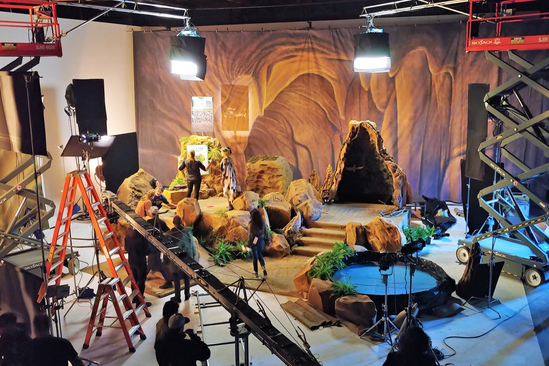 A canyon set with sculpted rock and a pool, lit from scissor lifts