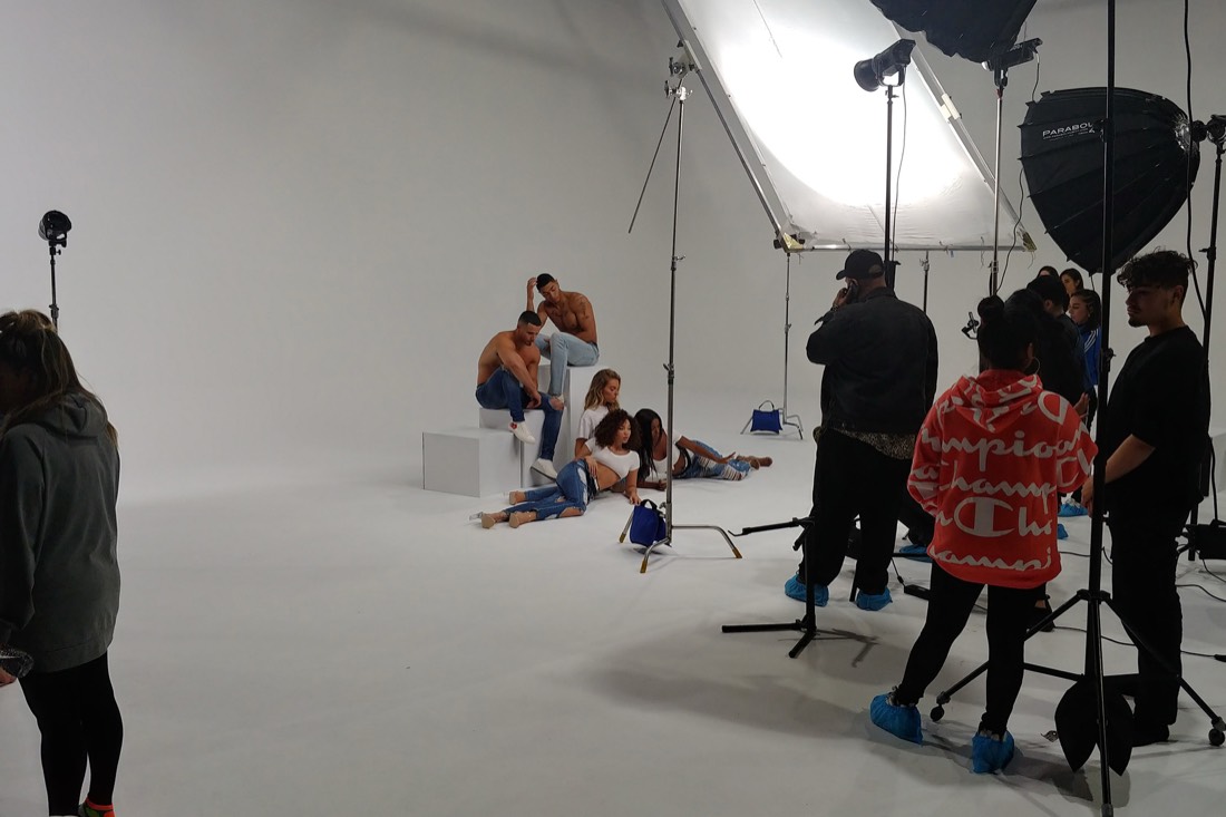 A photo shoot on the white cyc with crew and lighting stands