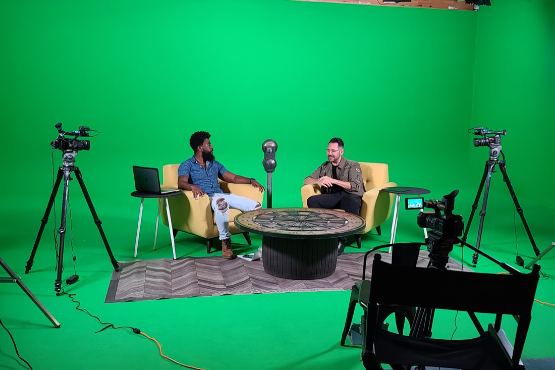 Two hosts on yellow chairs recording a show on the green screen