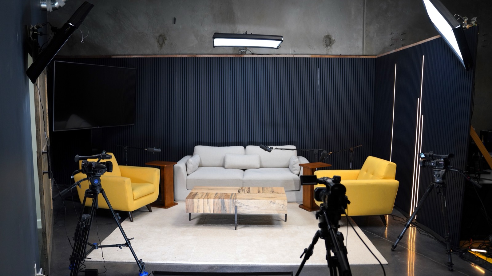 The podcast room set with a sofa, two armchairs, and three cameras