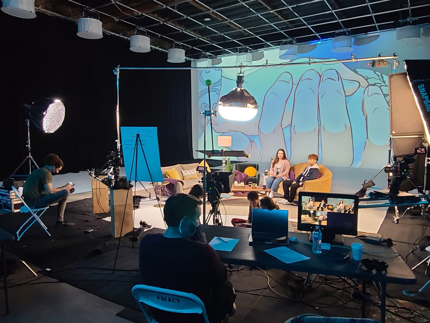 A dressed talk set with a painted backdrop and crew at video village